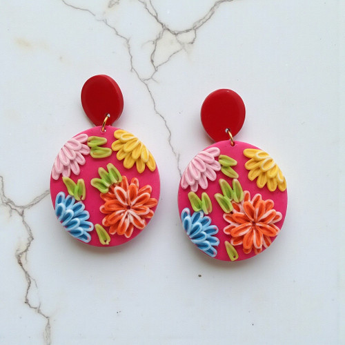 Pair of handcrafted fuchsia pink polymer clay earrings with vibrant 3D sculpted flowers in orange, blue, and yellow.