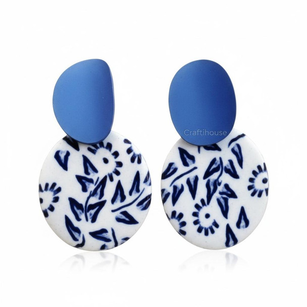 A pair of handcrafted white circular clay earrings featuring a cobalt blue Chinoiserie botanical pattern and matching bold blue studs.