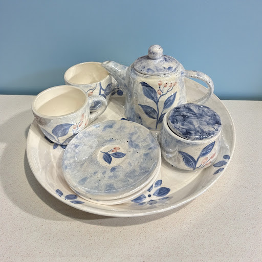 A 7-piece hand-painted ceramic tea set featuring blue botanical designs on a speckled white glaze.