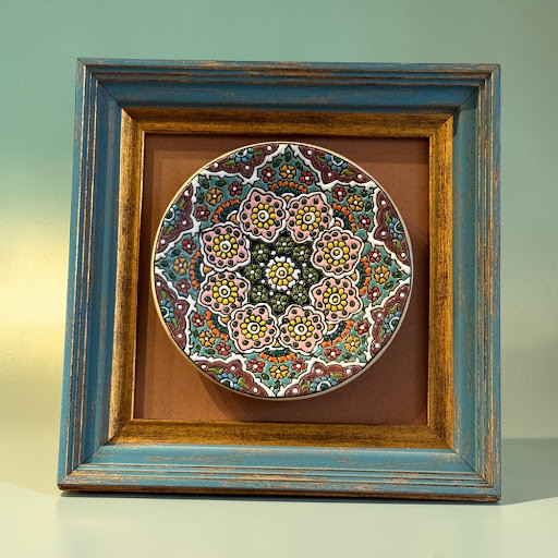 A 16 cm embossed painted pottery plate featuring a sunburst motif, mounted in a 25x25 cm wooden frame.