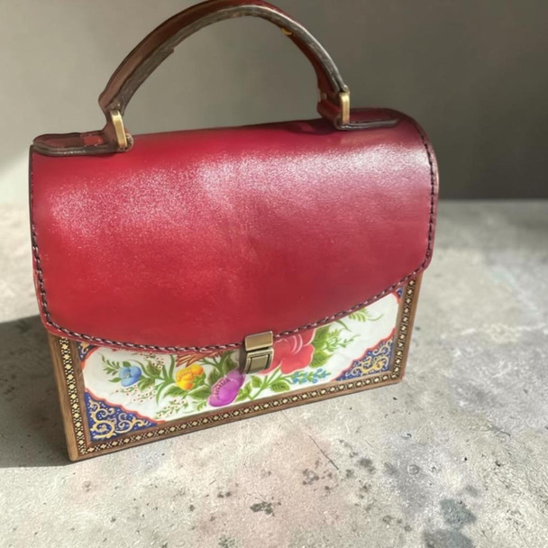 A luxury red leather and wood handbag featuring a hand-painted floral front panel and intricate Khatamkari borders, presented as a special gift.
