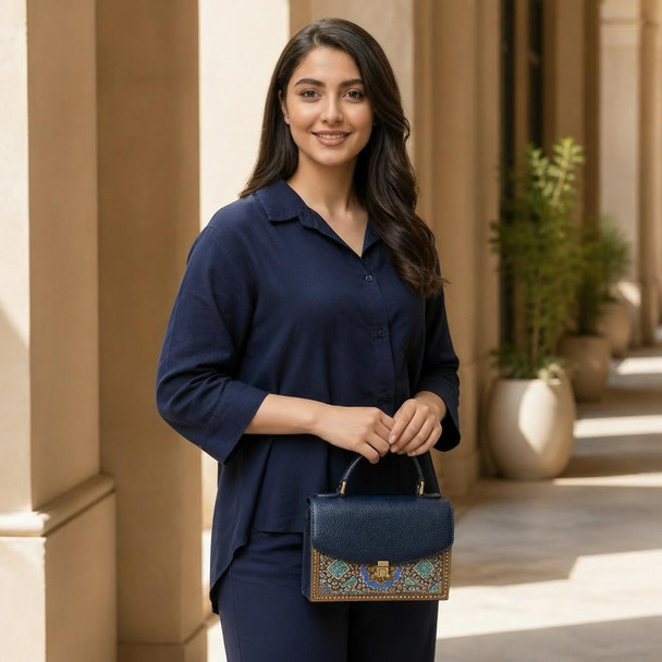 A  genuine cow leather structured handbag featuring an ornate gold scroll pattern and a secure clasp on a neutral surface.