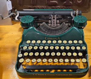 Front view of a vintage green Corona portable manual typewriter with round cream glass keys, black ribbon installed, and classic metal construction.