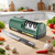 Kitchen countertop layout showing a chef knife resting next to the green 3-stage electric knife sharpener surrounded by fresh vegetables