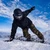 Lifestyle action photo of a snowboarder carving on the XCMAN Men's Snowstorm Night Snowboard down a snowy mountain slope under a blue sky
