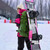 A snowboarder carrying a snowboard equipped with XCMAN 360 Seco bindings in a snowy mountain resort setting