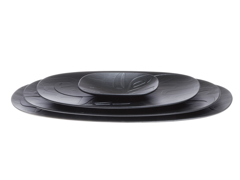 Four black oval nesting platters, etched with a West Coast First Nations abstract design.