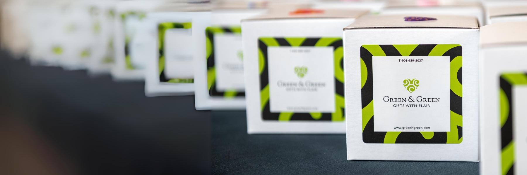 A row of small white gift boxes with green and black Green &amp; Green | Gifts with Flair logo stickers.