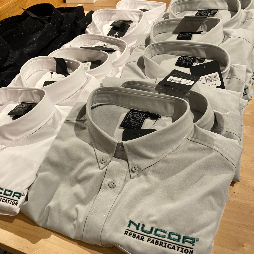 Branded merchandise shirts. the colors are black, white and gray. There is the logo of Nucor Corp on the left side of the chest.