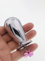 Hand holding a mushroom-shaped aluminum butt plug, showcasing its compact size and attached pink chimes.