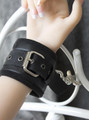 Close-up of black leather plush-lined handcuff fastened to a wrist and attached to a metal bed frame