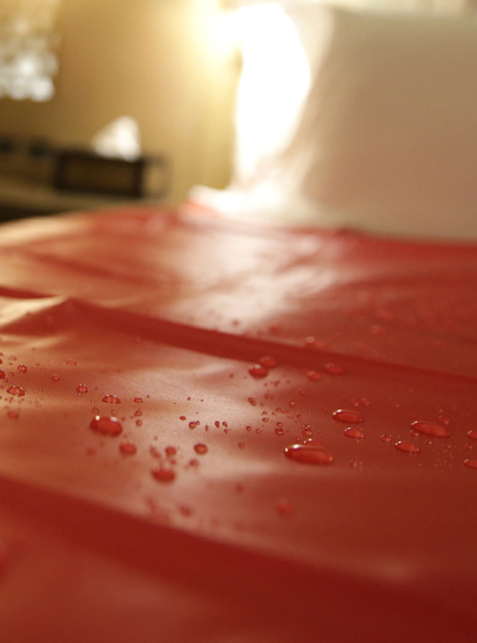 Waterproof sheet laid over a hotel bed, glistening with water droplets.