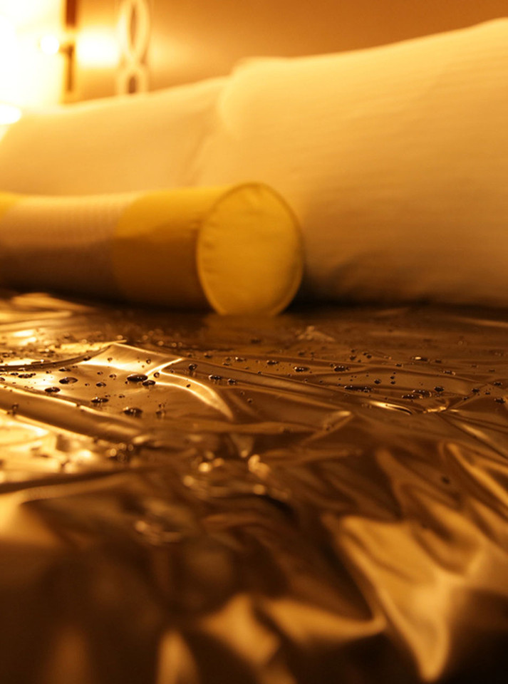 Waterproof sheet laid over a hotel bed, glistening with water droplets.