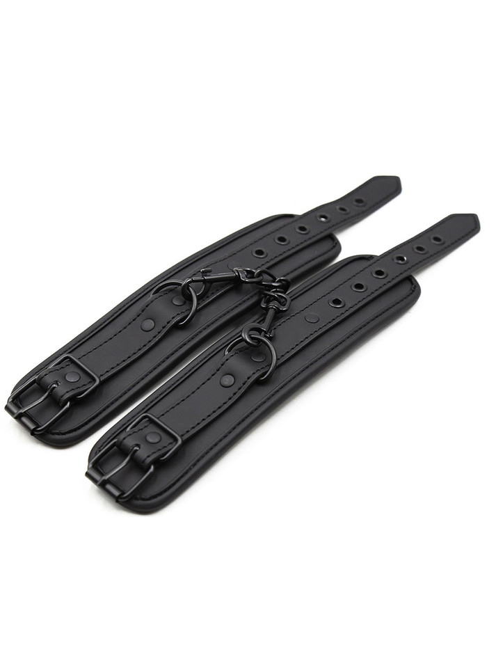 Flat lay of black leather restraints showing adjustable straps and connecting rings with matte black finish