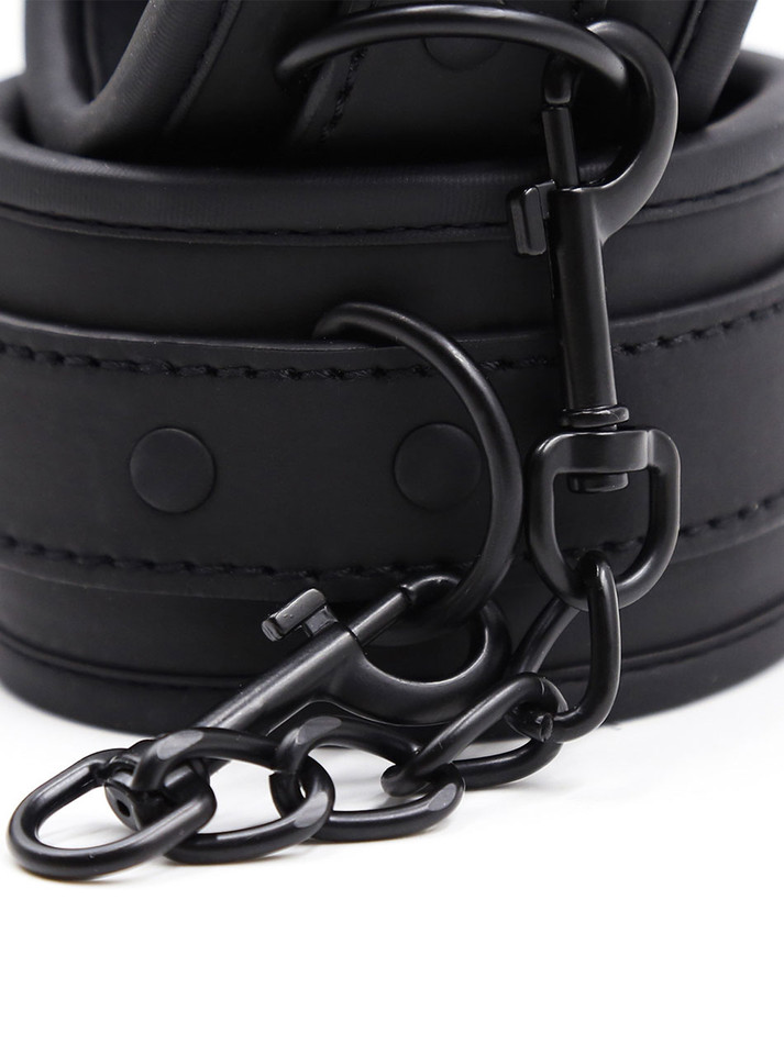 Detailed close-up of black metal chain and D-ring connection on leather bondage restraint