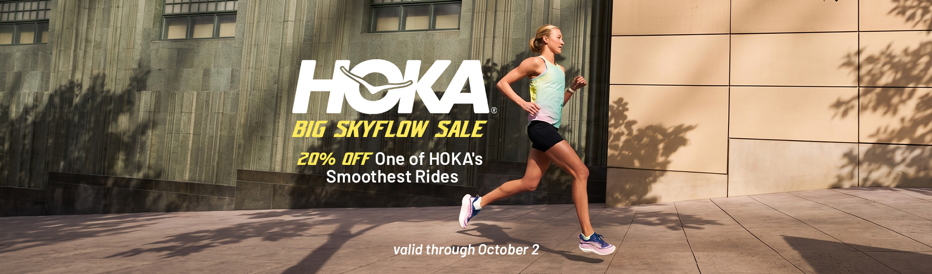 graphic, a blonde woman running on a paved city plaza past a large stone building wearing a pastel gradient tank top, black shorts, and pink and blue HOKA running shoes, text, HOKA BIG SKYFLOW SALE: 20% OFF One of HOKA's Smoothest Rides! valid through October 2