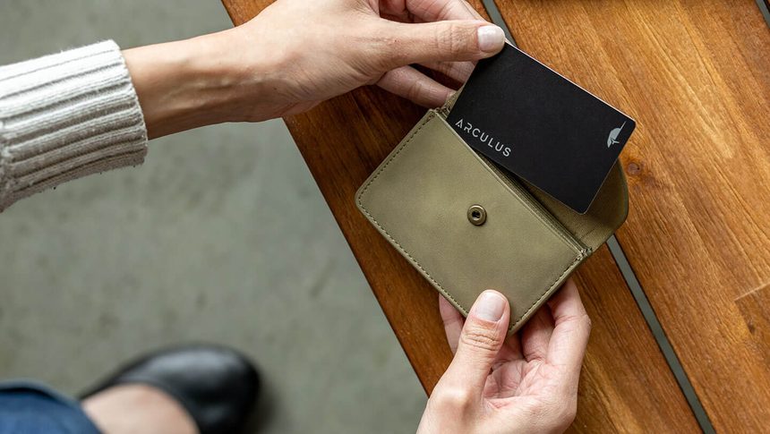 Hand placing the Arculus card into a wallet on a wooden table