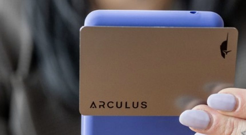 Hand holding the gold Arculus metal card in front of a person using the Arculus app