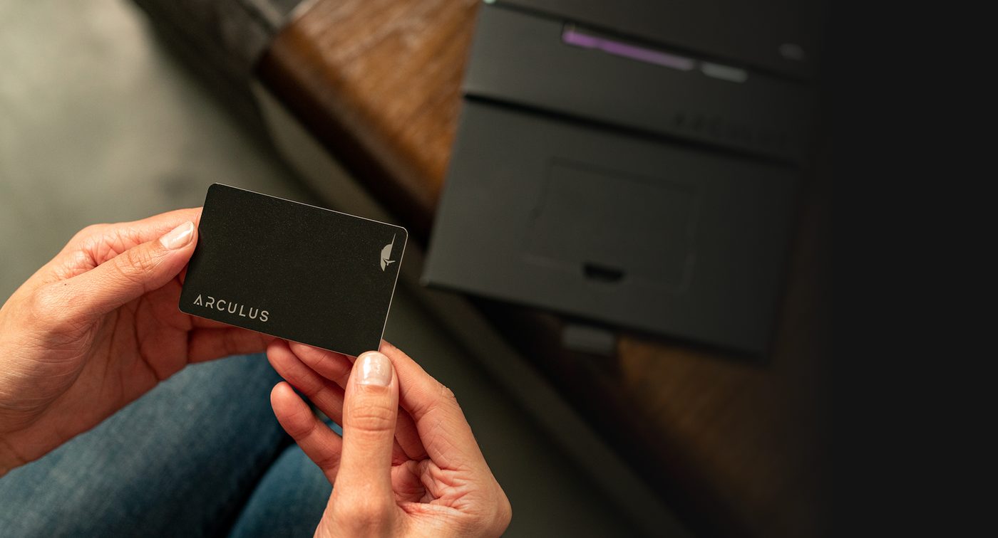 Hand holding the black Arculus card with the Arculus icon in the background