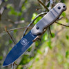 The ESEE Laser Strike (ESEE-LS-P-TG) shown with its 4.75-inch 1095 plain edge spear point blade in a Tactical Gray finish and flat grind, tan Micarta handle with removable scales revealing the hollowed storage tang and bow drill divot, and its black Kydex sheath.