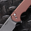 Pro-Tech Mordax BSA26.Mordax.1 shown open with the brown aluminum handle prominently displayed against a dark diamond plate background. The solid brown anodized aluminum scales and white pearl button lock release are clearly visible, with the stonewash CPM MagnaCut blade extending from the frame.
