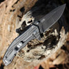 Close-up of the 8Cr13MoV drop point blade highlighting the black stonewash and dual thumb studs.
