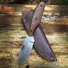 The ESEE Gibson Belt Knife (ESEE-EBK-M) shown with its 2.8-inch CPM-MagnaCut plain edge drop point blade in a satin finish, sculpted brown burlap Micarta handle, and its brown leather sheath.