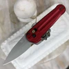 The Benchmade Lowden (491GY-01) shown with its 2.79-inch Böhler M390 spear point blade in a gray Cerakote finish and flat grind, milled Phoenix Red anodized aluminum handle scales, and its reversible tip-up pocket clip. The AXIS Lock flipper mechanism is visible along the spine of this compact, fidget-friendly EDC folder.
