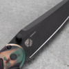 Pro-Tech Avalon PN1103-SHIPWRECK shown at an angle on a gray concrete surface, highlighting the spine and clip side of the knife. The black deep-carry pocket clip, black thumb studs, and the Shipwreck multicolor aluminum handle finish are visible from this perspective.