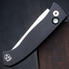 Pro-Tech Brend Classic BSA26.Brend.1 shown in a lengthwise profile against a dark walnut wood background, highlighting the knife's full silhouette in the closed or open position. The black aluminum handle, black pocket clip, and satin 154CM blade are visible from this angle.