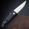 Pro-Tech Brend Classic BSA26.Brend.1 shown open against a dark walnut wood background, angled to display the full length of the knife from a slightly elevated perspective. The satin 154CM blade and solid black aluminum handle are both in frame, showing the overall proportions of the Brend 1 platform.