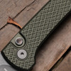 Close-up detail of the Pro-Tech Chaves Scapegoat Compact BSA26.Scapegoat.2 handle on a dark wood surface. The green carbide diamond crosshatch texture is shown in full detail, with the black lip pearl push-button release and blasted hardware clearly visible against the OD green aluminum scales.