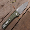 Pro-Tech Chaves Scapegoat Compact BSA26.Scapegoat.2 shown at an elevated angle on a dark wood surface, displaying the spine and handle profile of the deployed knife. The green carbide-textured aluminum scales and blasted hardware are prominent from this perspective, with the acid wash blade extending from the frame.