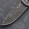 Close-up of the Pro-Tech VERO Synapse 2 Custom 002 Chad Nichols Raindrop Damascus blade on a gray slate surface. The distinctive concentric swirling raindrop pattern of the Damascus steel is the focal point, showing the full width and depth of the pattern across the blade face.