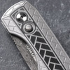 Close-up detail of the Pro-Tech VERO Synapse 2 Custom 002 handle on a gray slate surface. The deep herringbone milled texture and 2-tone blasted and tumbled finish of the 17-4 heat treated steel scales are shown in full detail, with the black lip pearl push-button release clearly visible against the textured handle.