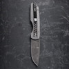 Pro-Tech VERO Synapse 2 Custom 002 shown from the clip side on a gray slate surface. The DLC machined titanium clip is prominently visible on the spine of the 17-4 herringbone steel handle, with the Raindrop Damascus blade partially visible at the base of the frame.