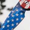 Pro-Tech TR-5 T501-PATRIOT shown at a closer angle against a blue sky background, emphasizing the blue field and white stars portion of the USA flag Patriot Cerakote on the handle. The full patriotic color scheme across the handle and CPM-S35VN blade is prominently displayed from this orientation.