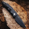 Pro-Tech TR-5 BSA26.TR5.1 shown at an angled profile on a rough stone surface. The feather-textured black aluminum handle, integrated steel glass breaker, black deep-carry pocket clip, and DLC black blade tip are all visible from this perspective, showing the full-feature TR-5 platform in the BSA26 configuration.