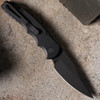 Pro-Tech TR-5 Operator T503-Operator shown open on a sandy concrete surface from a slightly elevated angle. The sterile DLC black blade is deployed, and the all-black aluminum handle, black hardware, and black deep-carry clip are fully visible with no identifying markings anywhere on the knife.