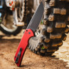 Pro-Tech Mordax Limited Edition MX103-LTD RED — open, flipper tab and pivot detail, solid red aluminum handle, dirt bike tire background