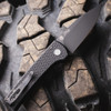 Pro-Tech Scapegoat Compact Auto RCS1106 — open, carbide textured black handle and push button detail, DLC black blade, cracked earth background
