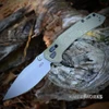 The Zero Tolerance 0203 (0203GRM390) shown with its 4-inch Böhler M390 drop point blade in a stonewash finish, 3D-machined Olive Drab Micarta handle over thick steel liners, and its black Cerakote reversible deep-carry pocket clip. The DuraLock crossbar with textured closing button and the solid pivot bolt are visible along the spine of this hard-use folder.
