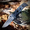 The Benchmade Adamas open, showing its 3.82-inch Tungsten Gray Cerakote CPM-MagnaCut drop-point blade with a partially serrated edge, black G-10 scales over full-length stainless steel liners, AXIS Lock, and black oxide deep-carry clip, alongside its black nylon MOLLE-compatible sheath.