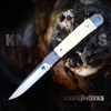 The CobraTec Trapper Hidden Release CTTHRPBWT is shown open on a dark, weathered piece of wood against a blurred background. The satin drop point blade carries a D2 stamp and the CobraTec logo, and the white bone handle sits between a polished steel end bolster and a checkered steel front bolster.