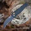 The Benchmade Kitsari 213BK-2601 is shown open, with its curved hawkbill blade extending from a black G10 handle milled in a radial pattern with Flat Dark Earth hardware.