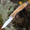 The Chris Reeve Mnandi (MNA-1008) shown with its 2.75-inch CPM MagnaCut hand-polished drop point blade, titanium handle inlaid with Box Elder Burl showing swirling grain patterns and rosy highlights, and its low-profile solid titanium pocket clip. The Reeve Integral Lock is visible along the handle, with the complete professional kit — wrench, grease, cloth, and G'Feller leather slip sheath — shown alongside the knife.