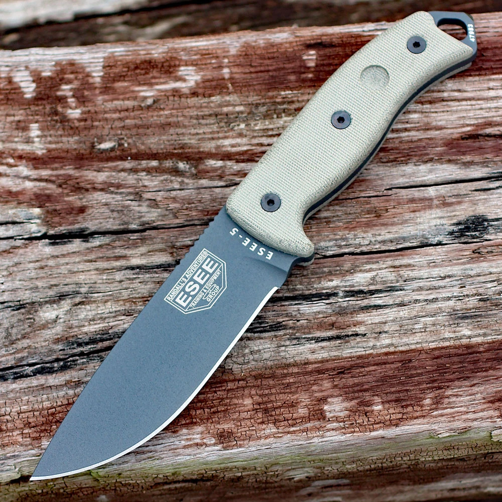 The ESEE-5 (ESEE-5P-TG) shown with its 5.25-inch 1095 saber ground drop point blade in a Tactical Gray finish, sharpened glass breaker pommel, fire-making bow drill divot, tan Micarta handle scales, and its black Kydex belt sheath.