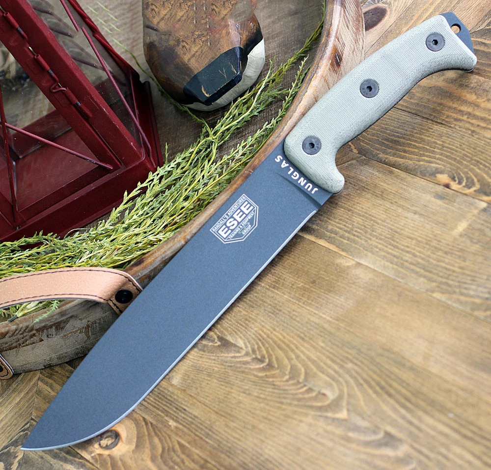 The ESEE Junglas (JUNGLAS-TG) shown with its 10.38-inch 1095 plain edge drop point blade in a Tactical Gray finish and flat grind, tan Micarta handle, and its black Kydex sheath with MOLLE back.