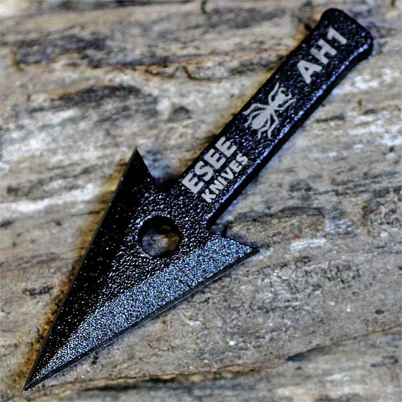 The ESEE AH-1 Arrowhead (ESEE-AH1), a black traction-coated 1095 steel double-edged blade shown with its tang nubs and hole cutout for mounting to a stick.