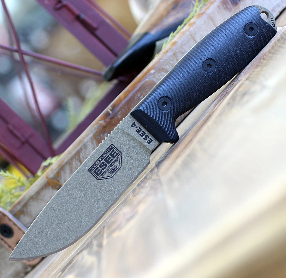 The ESEE-4 3D Handle (ESEE-4PDE-001) shown with its 4.50-inch 1095 drop point blade in a Dark Earth finish and tall flat grind, 3D black G-10 handle scales, and its injection-molded black polymer sheath.